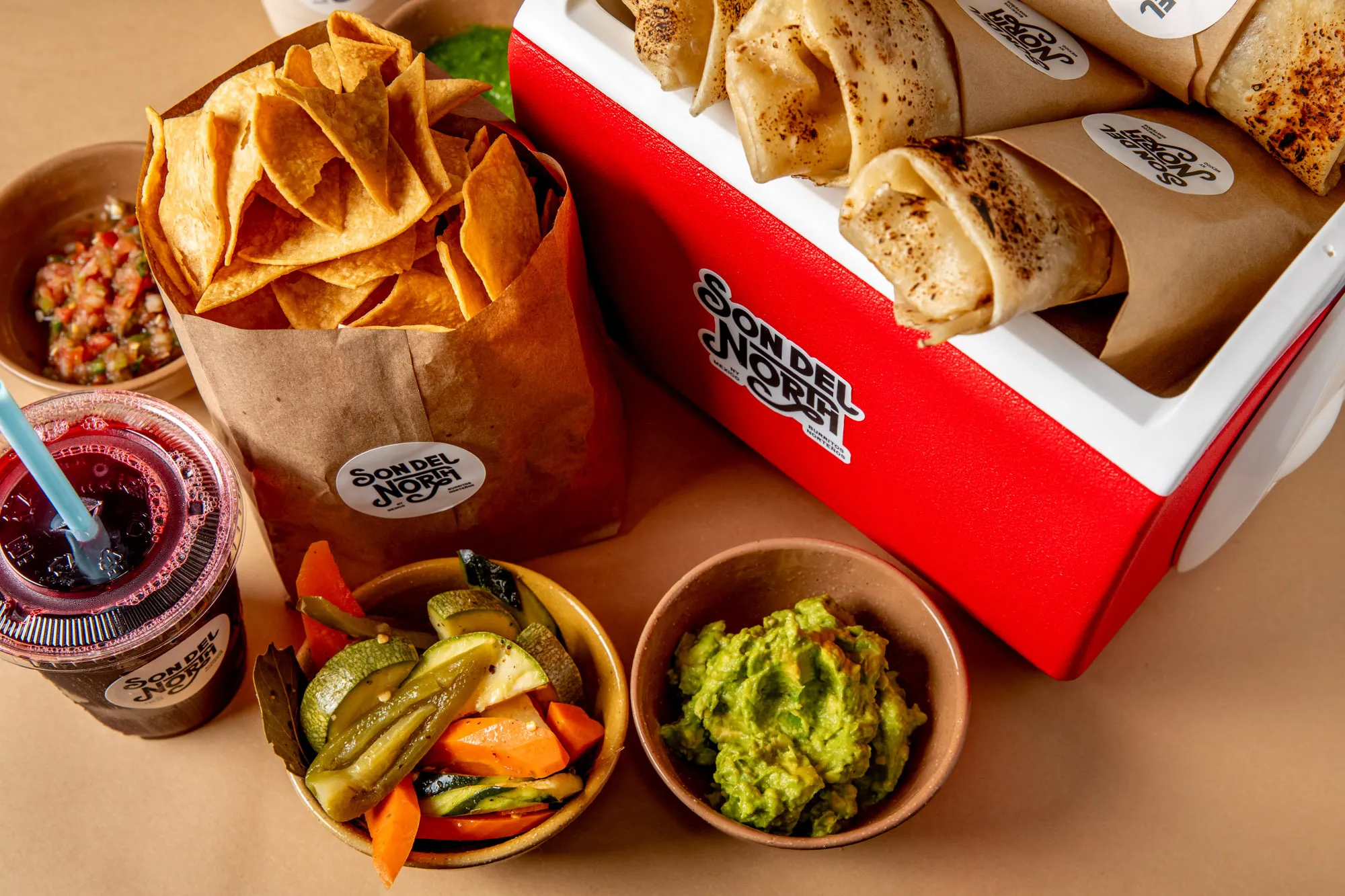 A table of offerings from Son Del North inlcuding salsa, chips, agua frescas and burritos