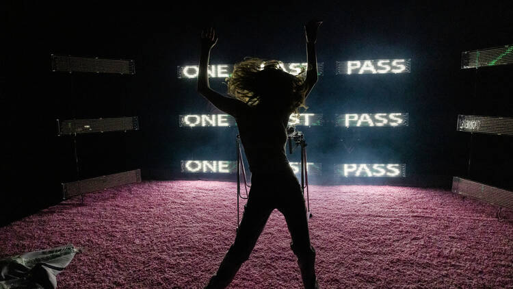 A woman dancing in front of a glowing neon sign.