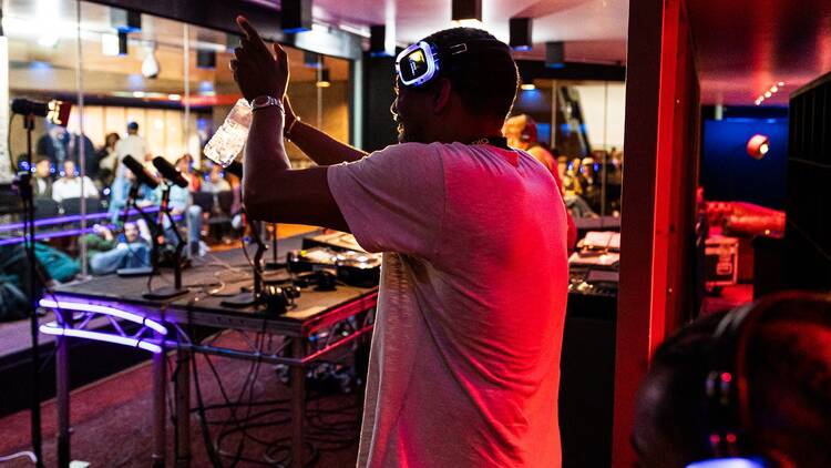 A man wearing headphones stands in front of a desk full of sound equipment during a live radio broacast at the Barbican as part of its Rebel Radio summer series 
