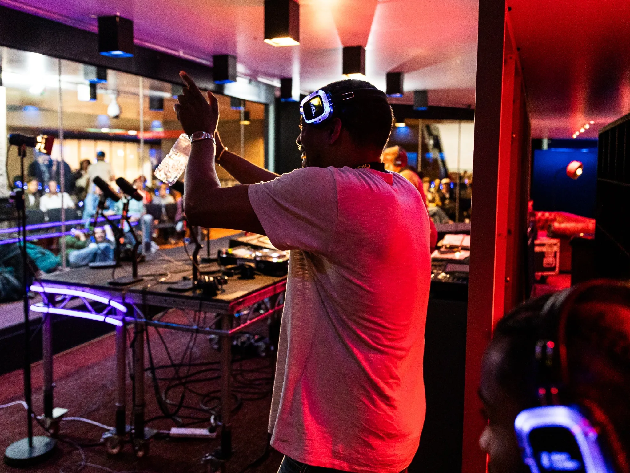 A man wearing headphones stands in front of a desk full of sound equipment during a live radio broacast at the Barbican as part of its Rebel Radio summer series