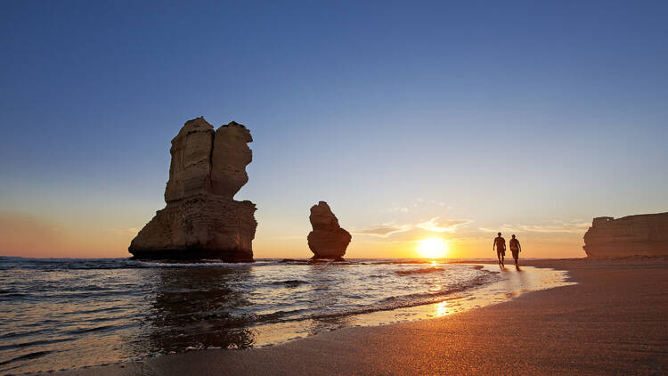 Couple hike past the Twelve Apostles at sunset