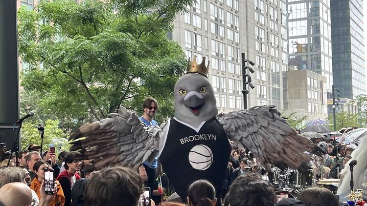 A person dressed up in a pigeon costume spreads its wings in front of a crowd.