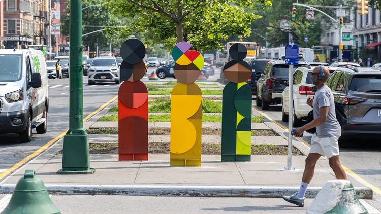 Three colorful sculptures stand on a sidewalk in Harlem.
