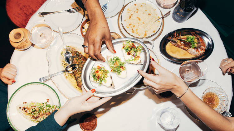 People passing plates of food over a large table with a white tablecloth, centre plate holds three oysters