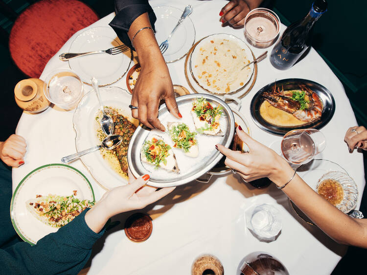 People passing plates of food over a large table with a white tablecloth, centre plate holds three oysters