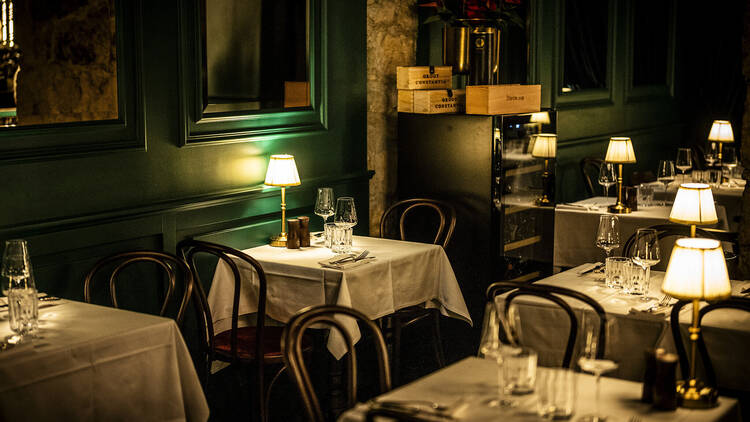 Dimly lit, cosy restaurant with tables with white tablecloths and individual lamps on tables, dark green walls