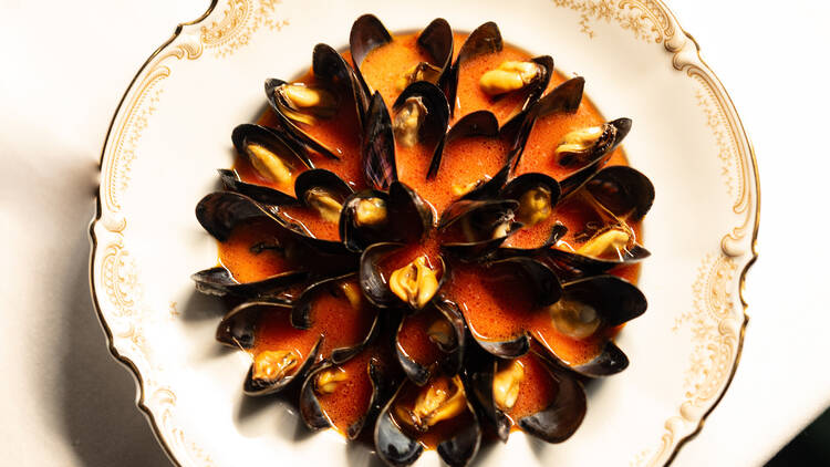 A bowl of mussels in an orange broth
