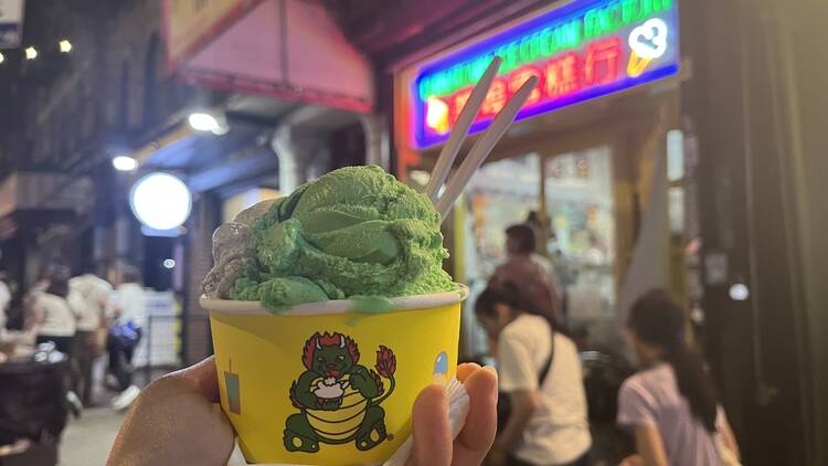 A hand holding a yellow cup with a dragon on it with a green scoop inside