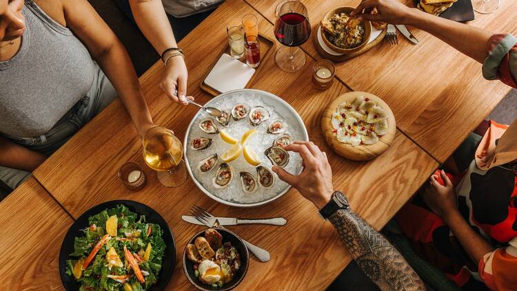 An overhead shot of people eating oysters and salads on a wood table