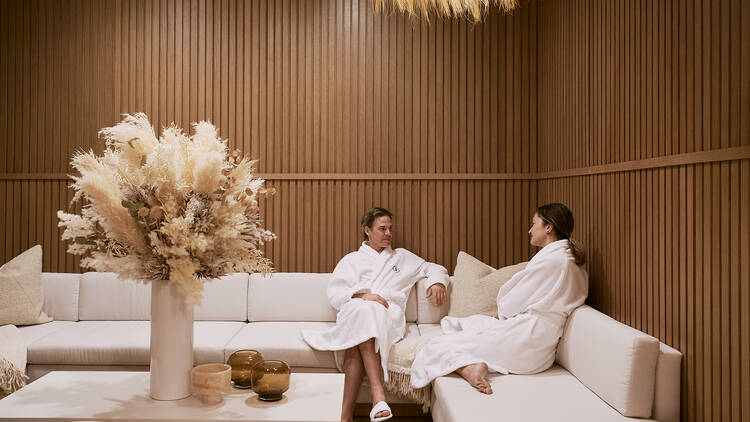 A couple sits inside a spa, wearing robes.