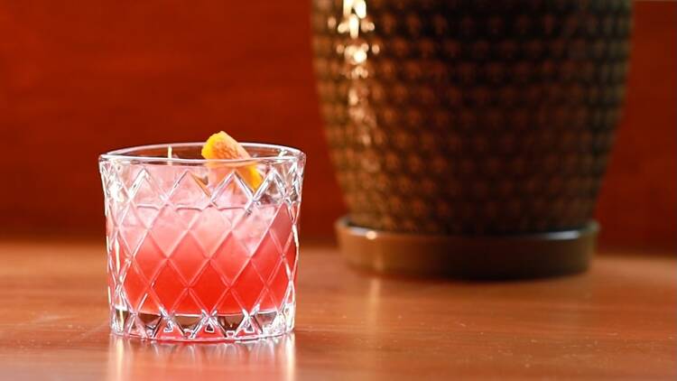 A reddish cocktail in a rocks glass on a wooden table