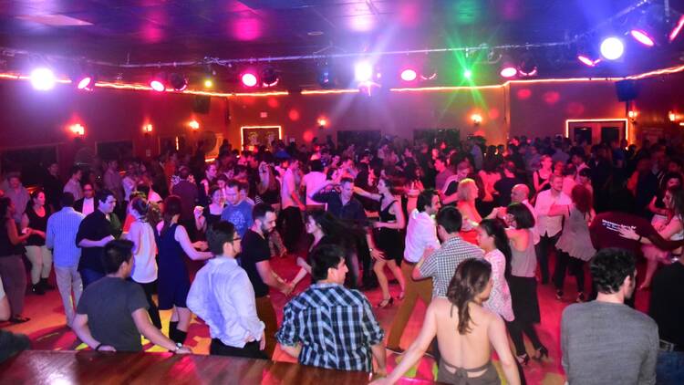 A crowd of people dance in a room under multi-colored lights