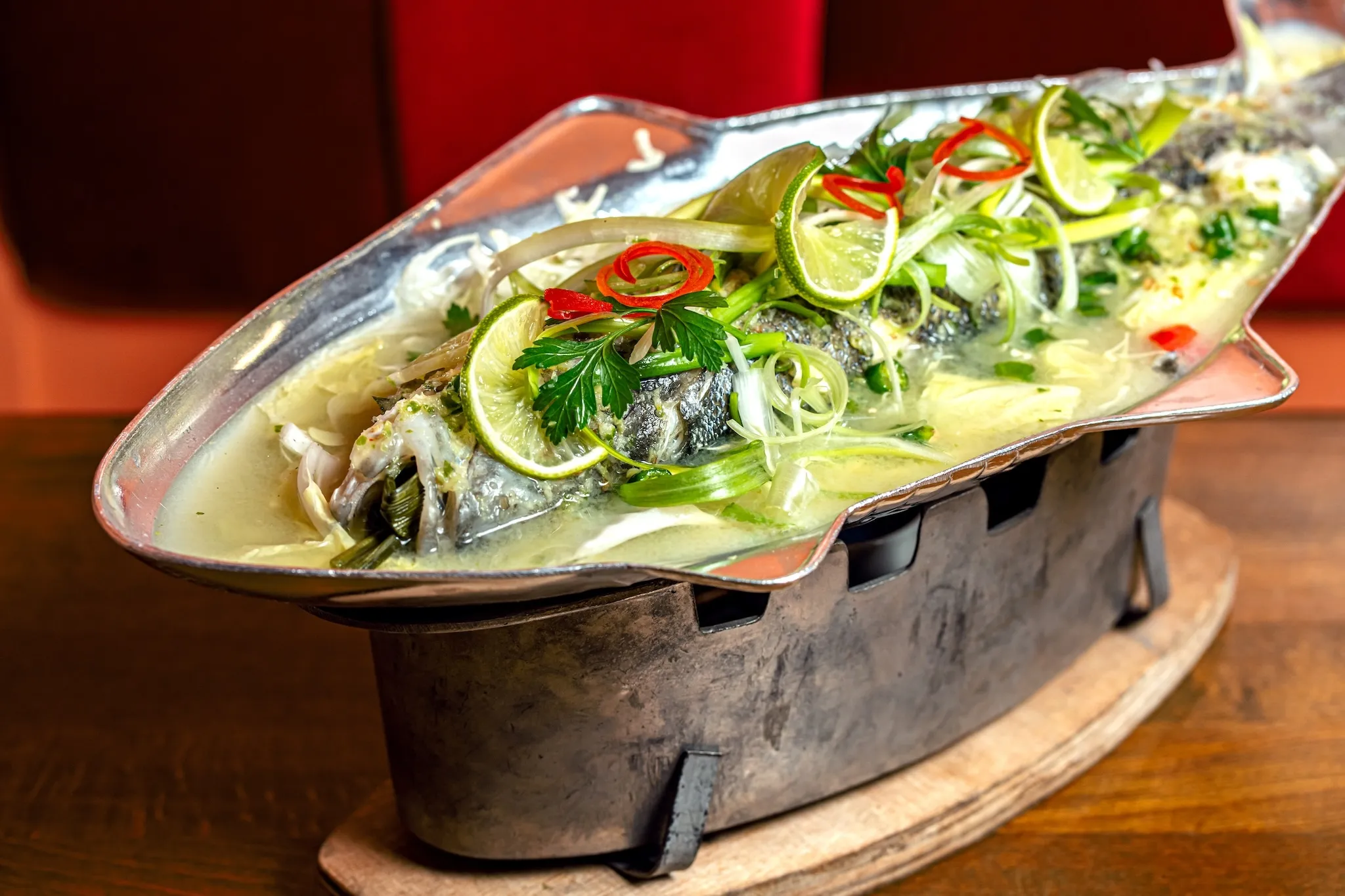 A whole fish covered in chiles served in a silver fish shaped bowl