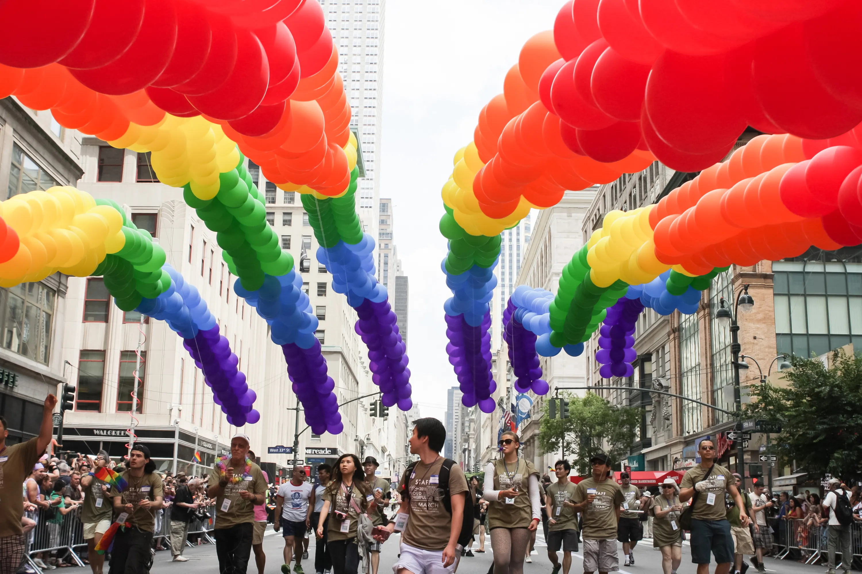 Colorful rainbow balloons float over a crowd at the NYC Pride March.