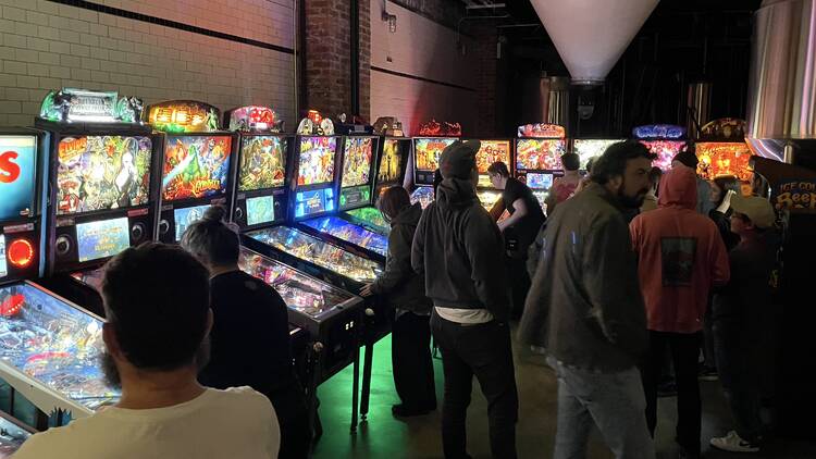 People gather around pinball machines to play.