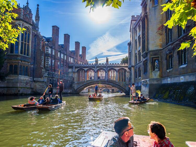 A vibrant scene on Cambridge’s River Cam, with people punting near historic university buildings, framed by the iconic Bridge of Sighs and autumn foliage.