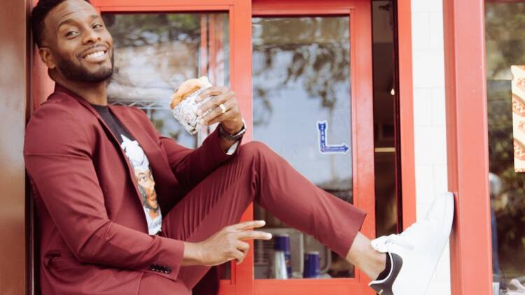 Actor Kel Mitchell sitting on a drive-thru window holding a burger