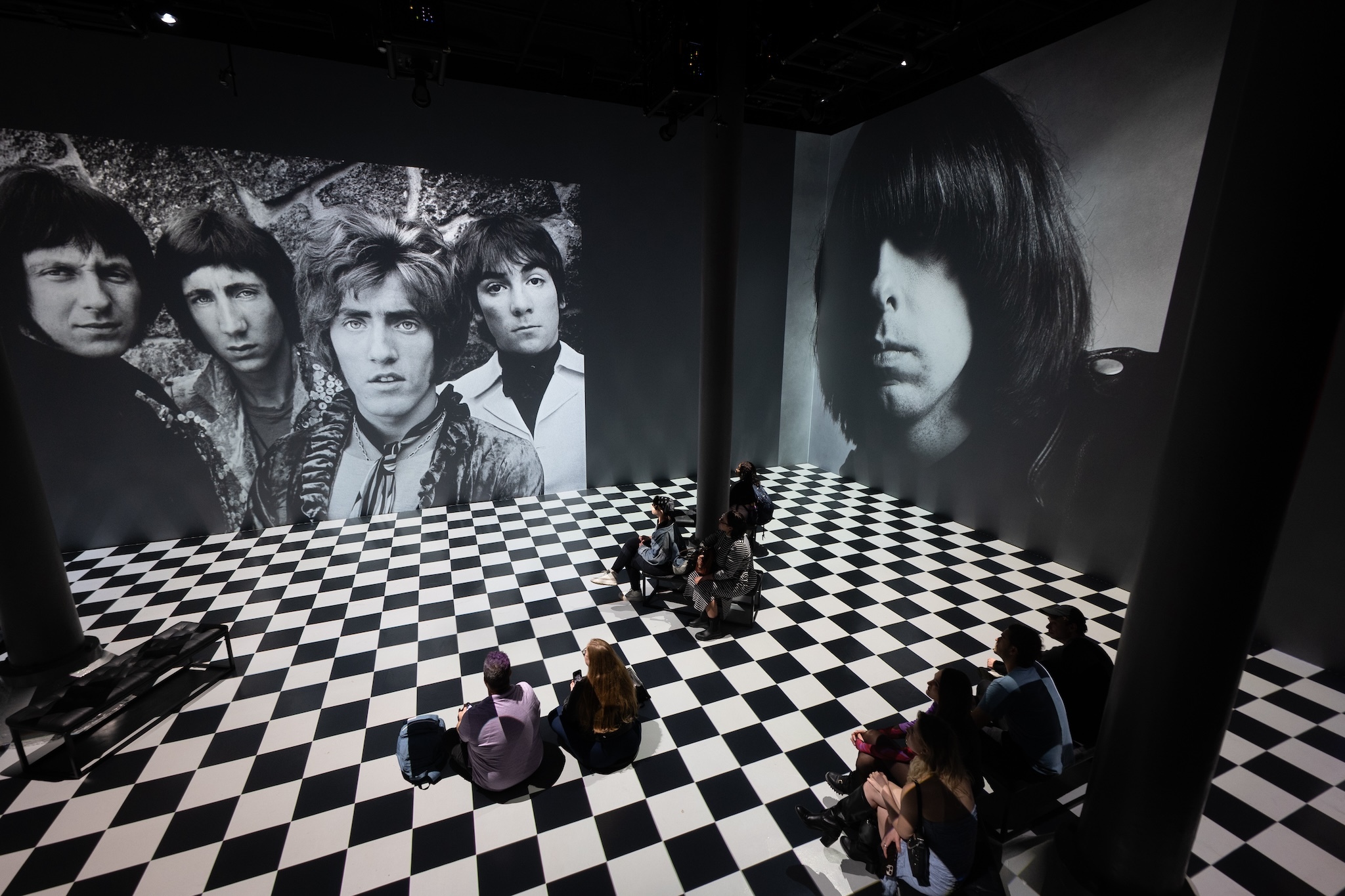 Black-and-white photographs of musicians are projected on a wall; the floor is black-and-white checkerboard.