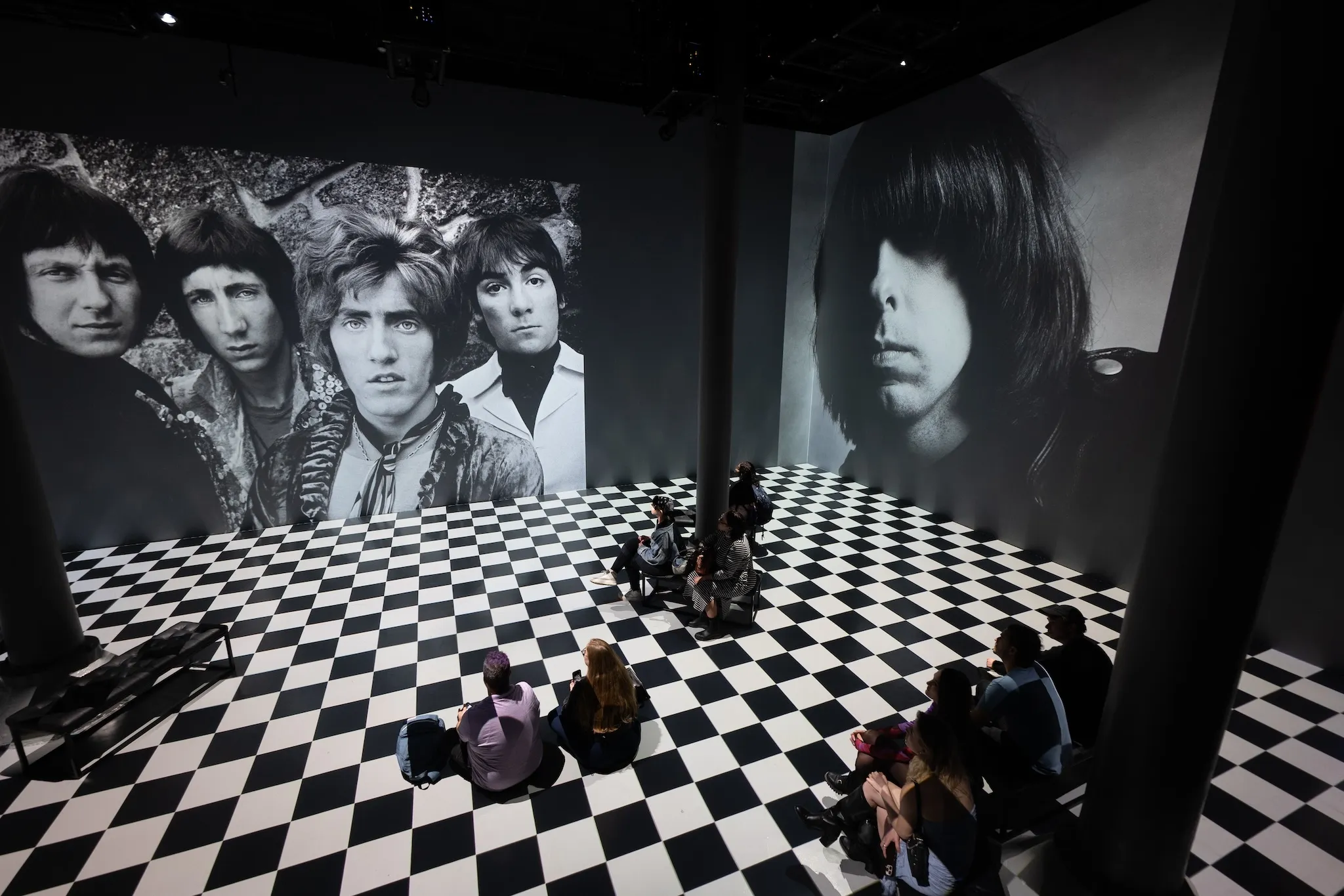 Black-and-white photographs of musicians are projected on a wall; the floor is black-and-white checkerboard.