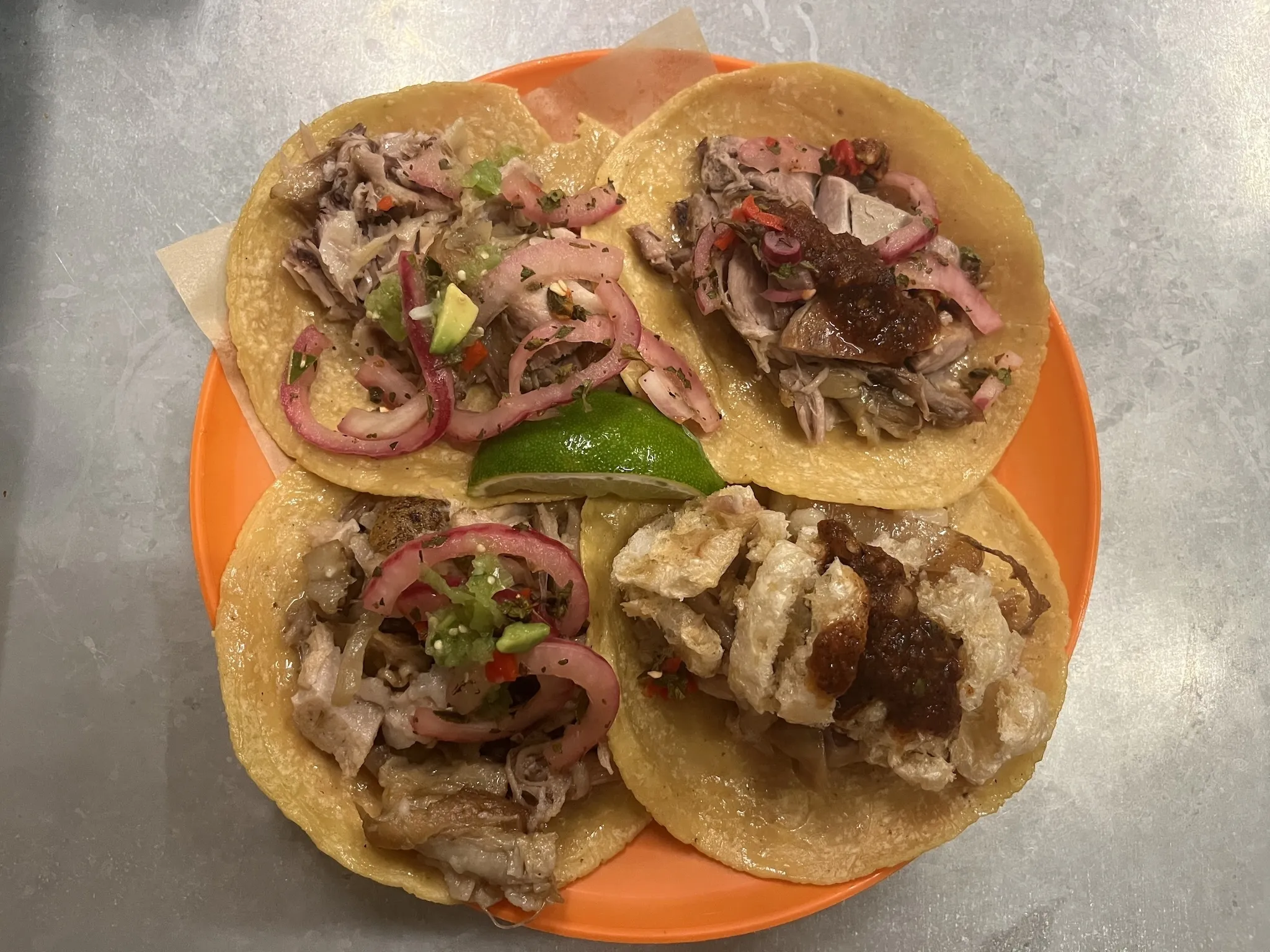 An orange plate with four pork tacos