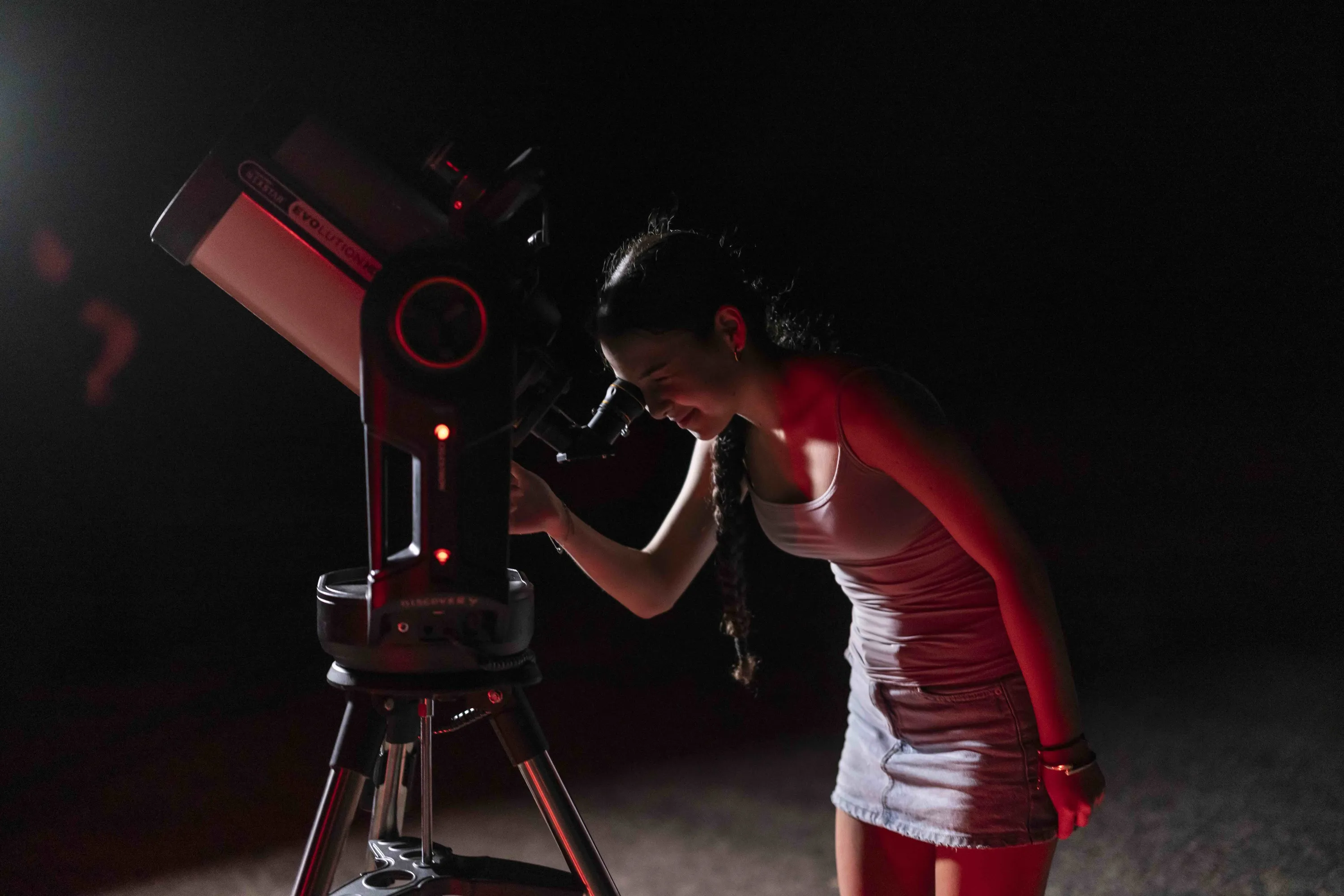 Girl stargazing through telescope at night