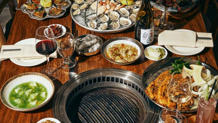 A table with a grill on it filled with crudo, a seafood tower and a kimchi pancake