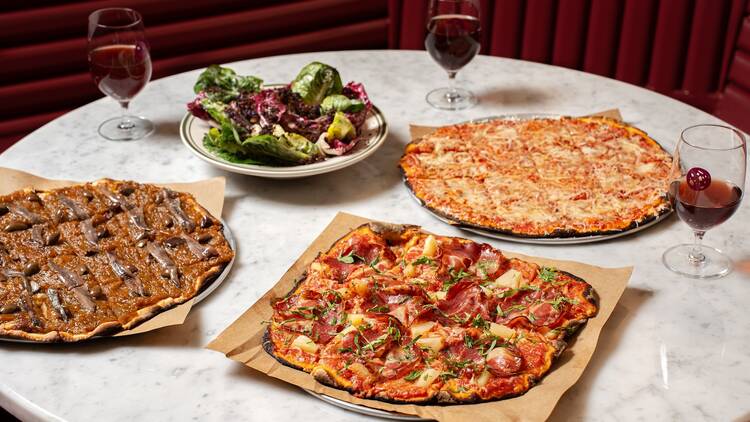 A table with three pizzas, a salad and wine