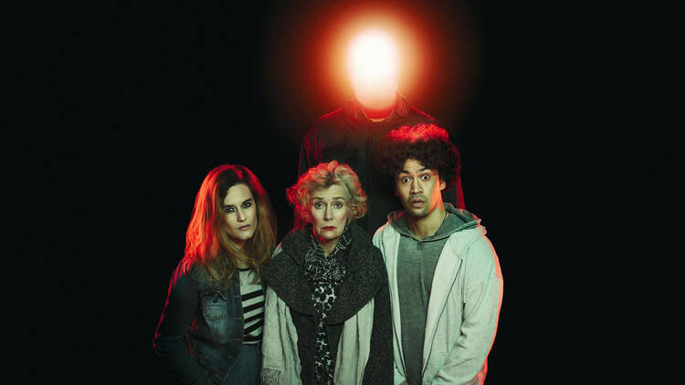 Four people posing in front of a black backdrop with a red light