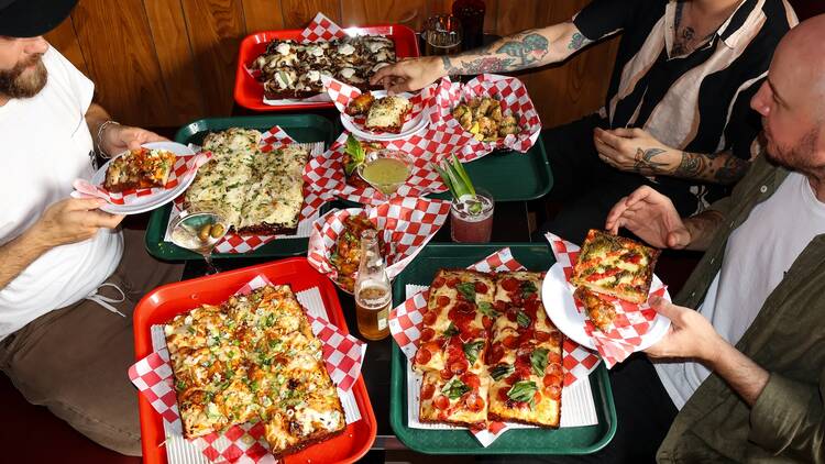Four people sitting around a table full of Detroit-style pies
