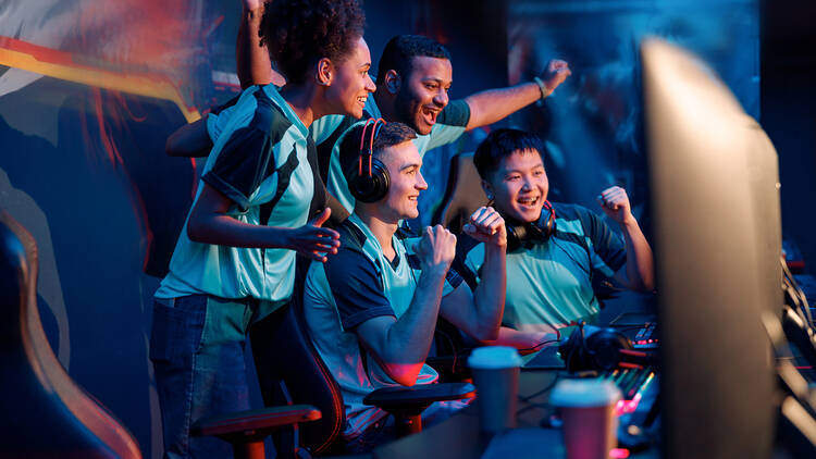 Multiracial cybersport gamers expressing success while raising hands up and smiling during participation in esports tournament in computer club
