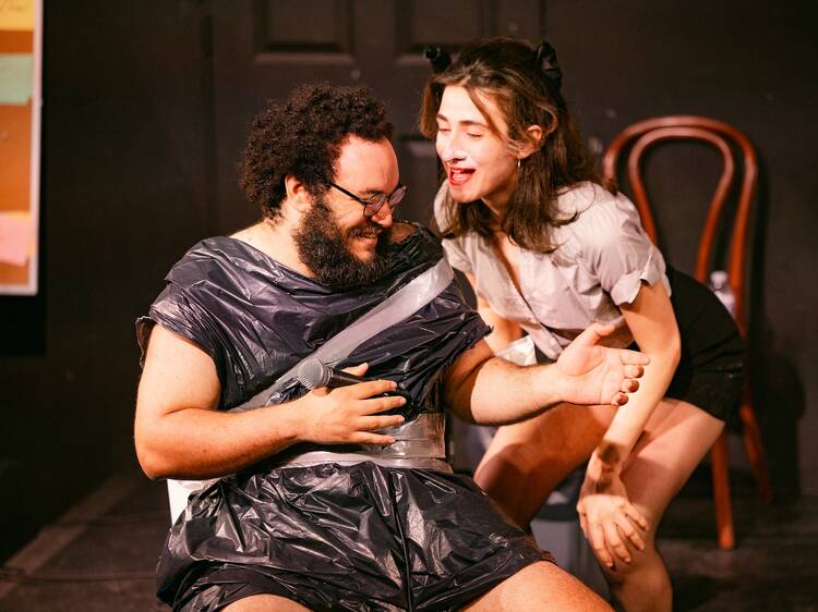 Two people on stage at a comedy show; one dressed as a raccoon and the other in a garbage bag