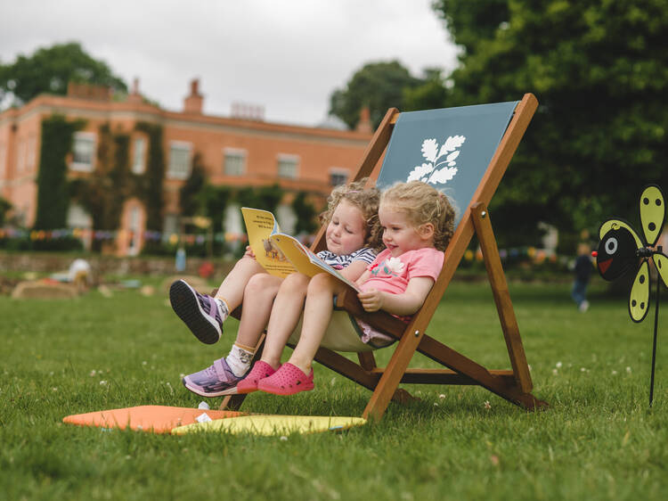 Children reading books in the deckchairs during the Summer of Play event at Killerton, Devon