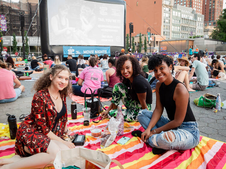 A group of young women sit on a picnic blanket watching a movie.