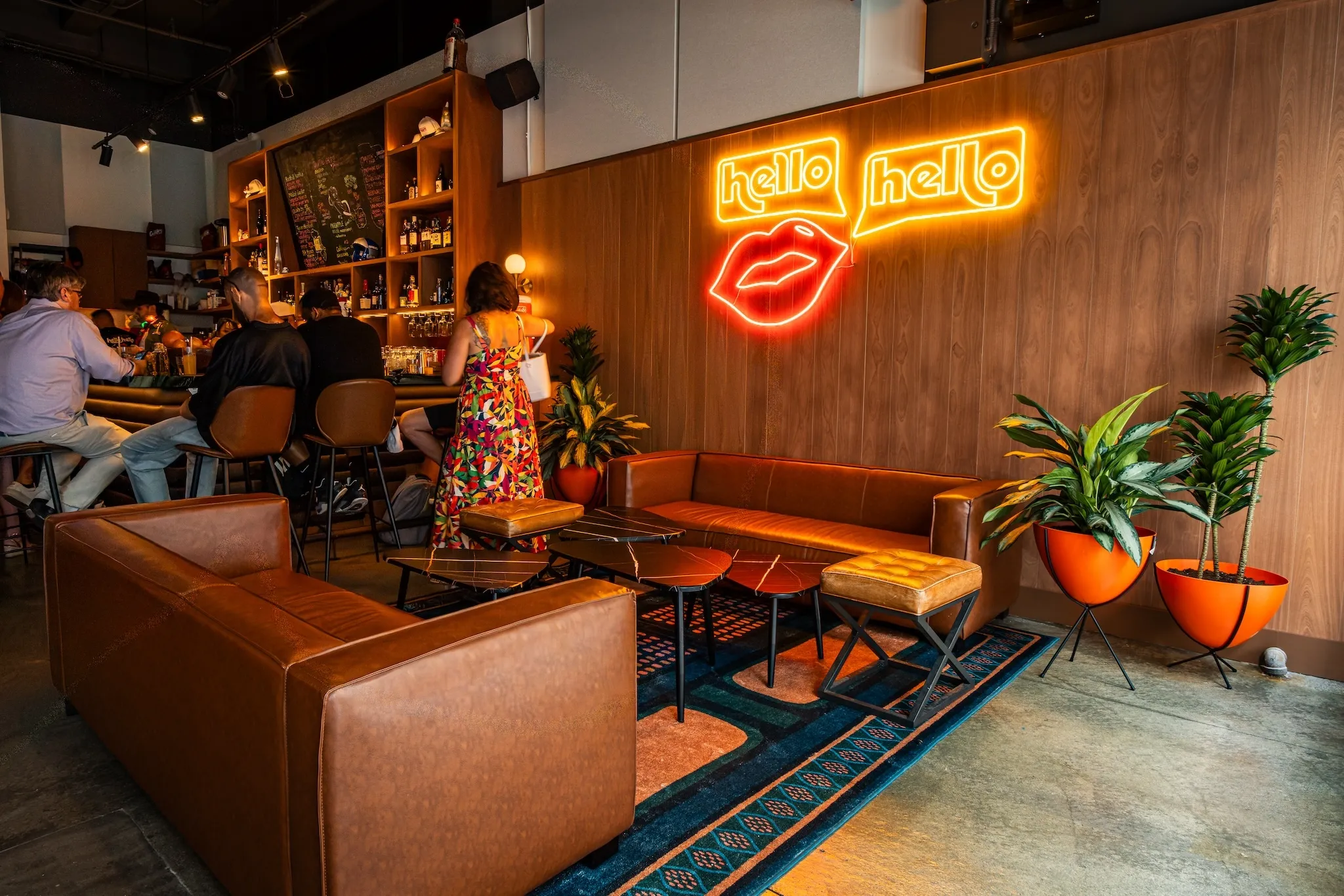 Two tan leather couches and wood paneled walls. The neon sign on the wall reads "Hello Hello"