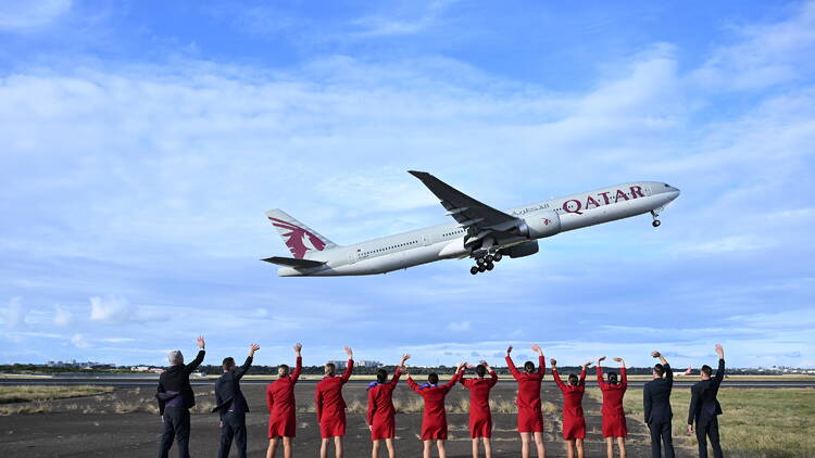 A Qatar Airways taking off with cabin crew waving from the ground.