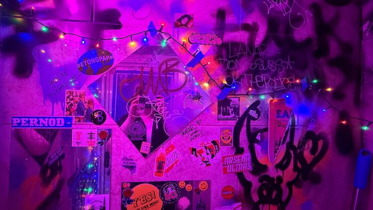 A heavily graffitied bathroom wall featuring a variety of stickers and a square mirror