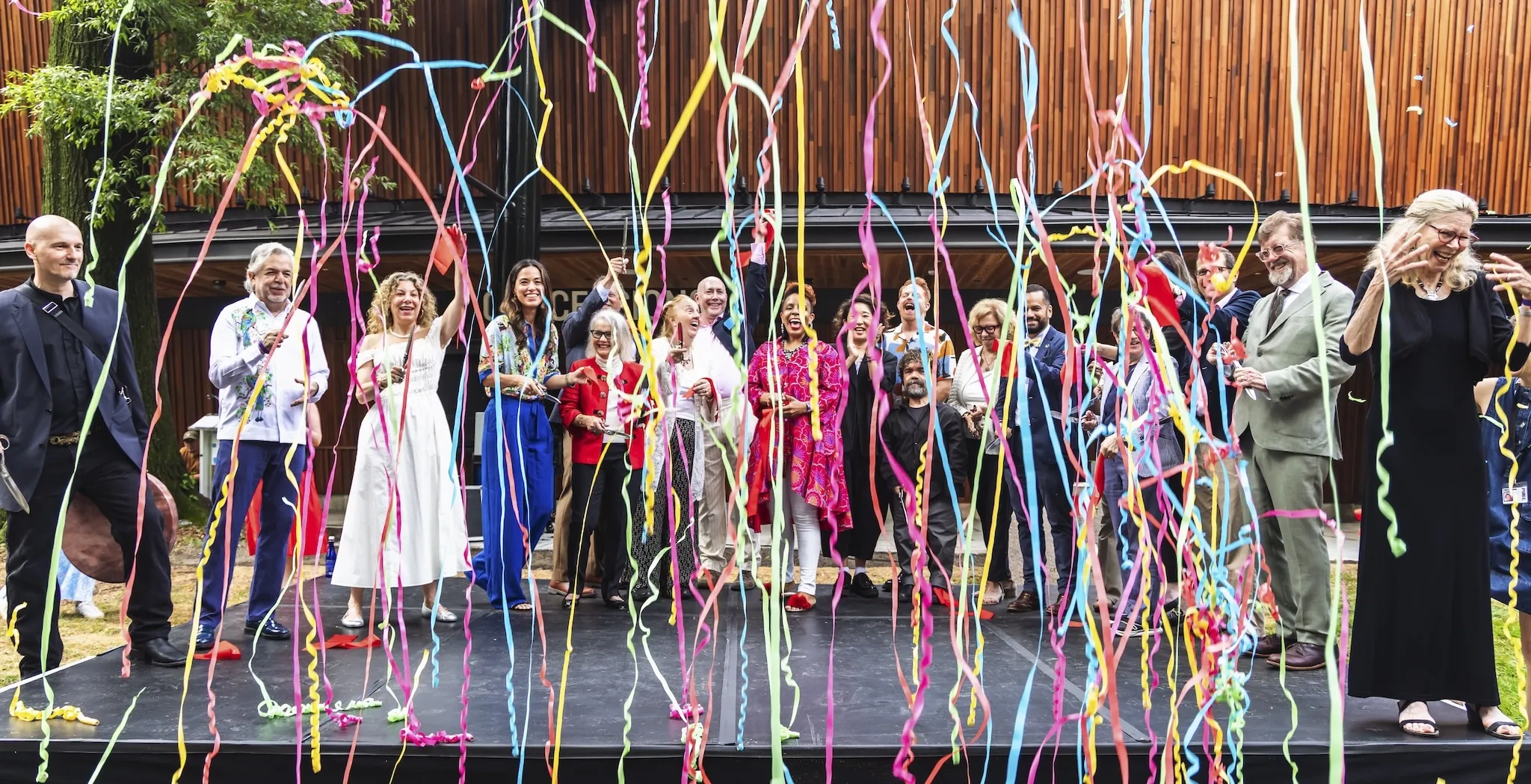Colorful confetti surrounds people on a stage during a ribbon cutting ceremony.