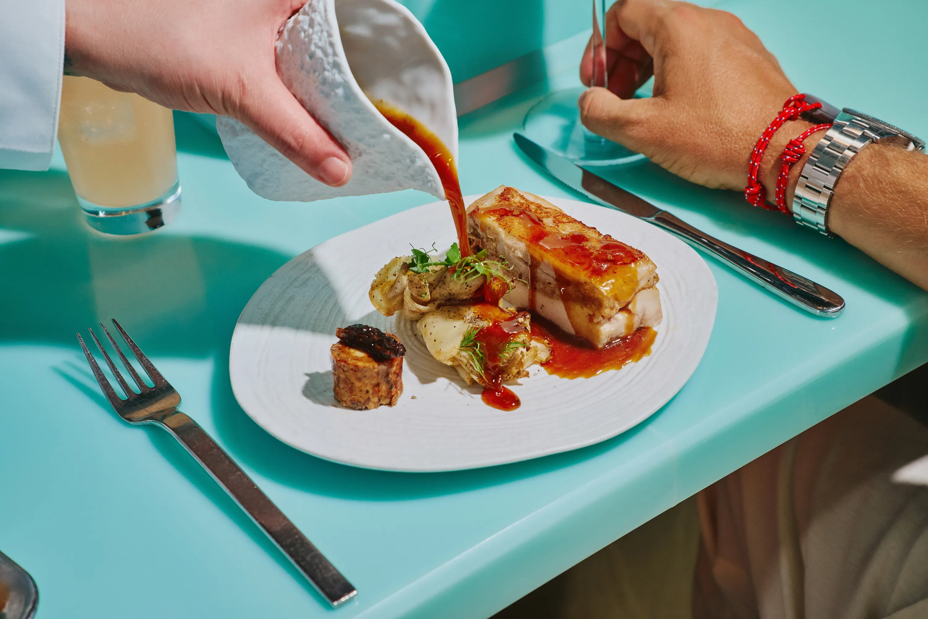 A person pouring au jus over the chicken dish