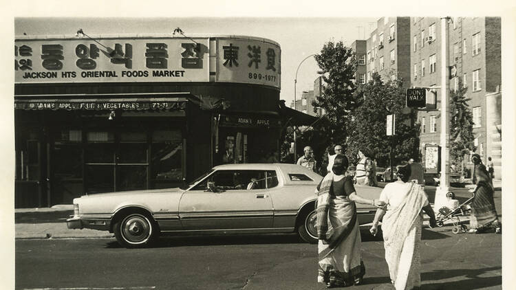 Two women wearing saris cross the street toward a car in a vintage photo.