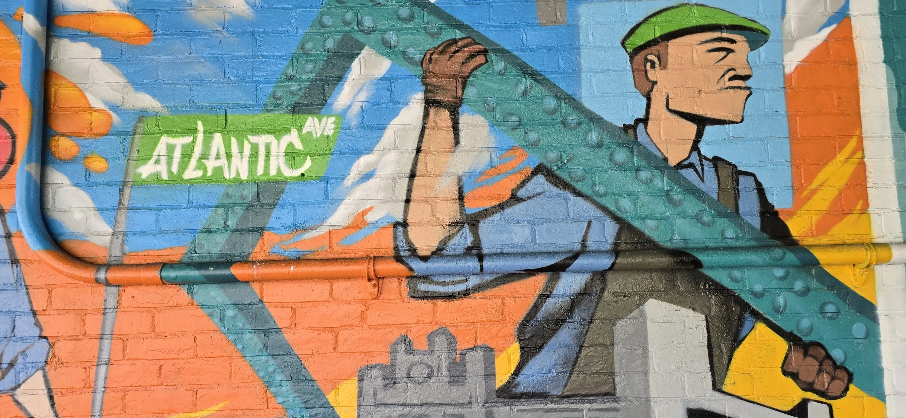A mural of a construction worker carrying a steel beam behind a street sign that says Atlantic Ave