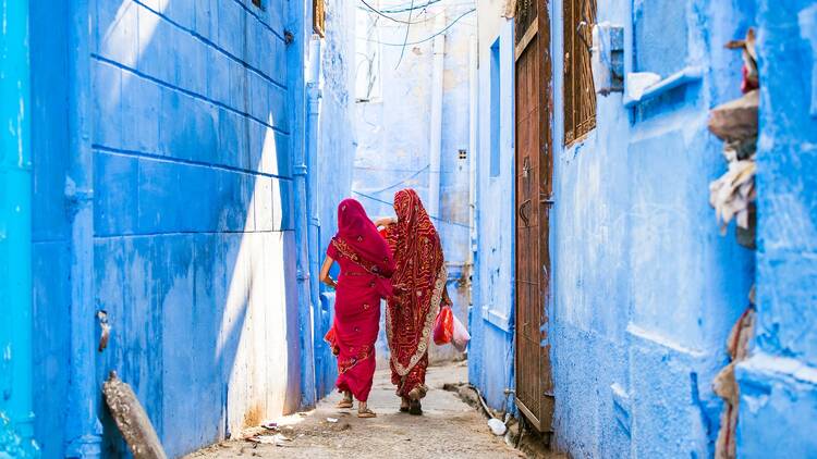 Two women dressed in the traditional Indian Saree are walking through the narrow streets of the blue city of Jodhpur, Rajasthan, India.