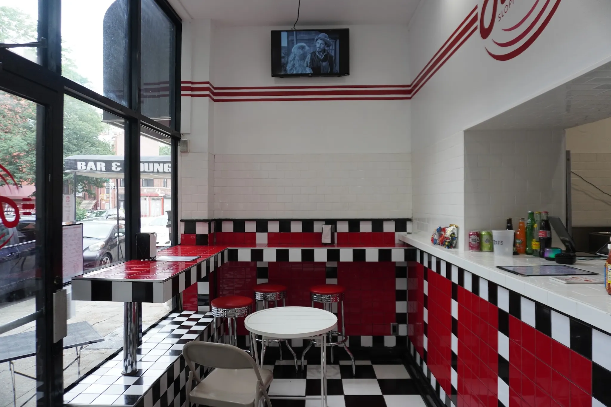 The interior of Farley's with features black and white tiles that line the floor and the walls, a handful of red stools inside and a window that looks into the kitchen