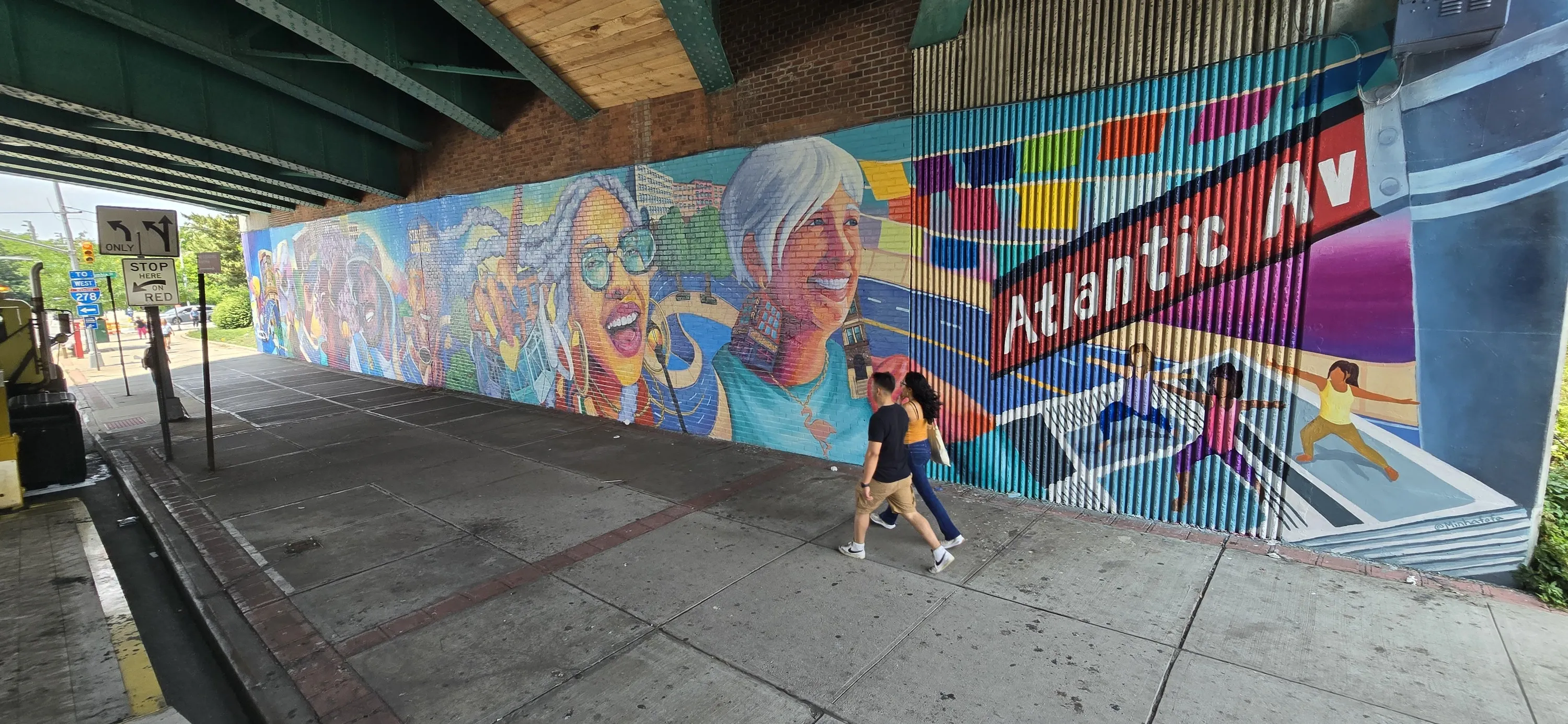 People walk by a larger mural under an overpass.
