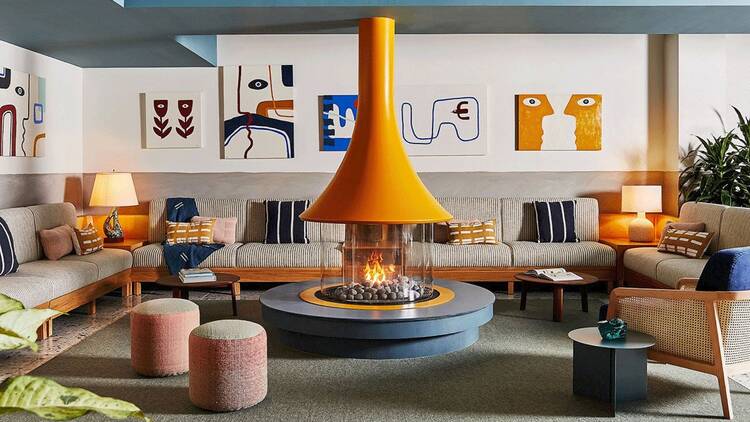 The lobby of a hotel with warm wooden tones and a Scandinavian-style fireplace.
