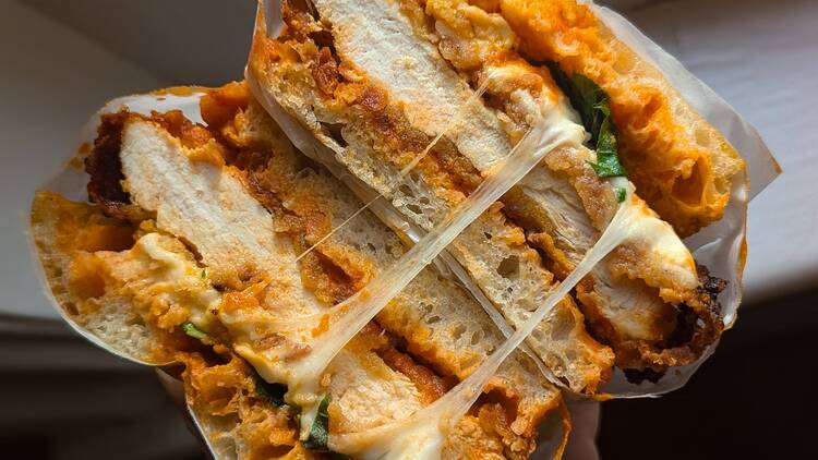 The Social Sandwich from Arcane Cross section of a large focaccia sandwich shoowing chicken, melted cheese and an orange sauce