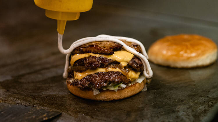 A juicy triple cheeseburger in the making at Tuning Burger — seared aged patties, melted cheese, and a swirl of house-made sauce.