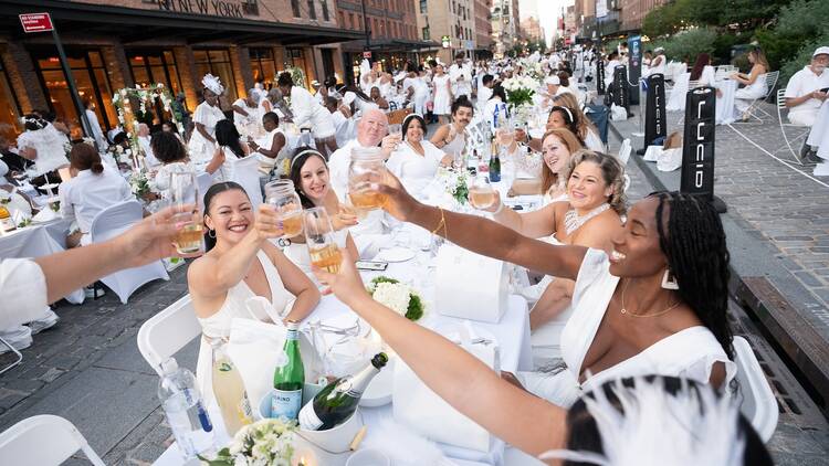 People wearing all white and cheersing with alcohol