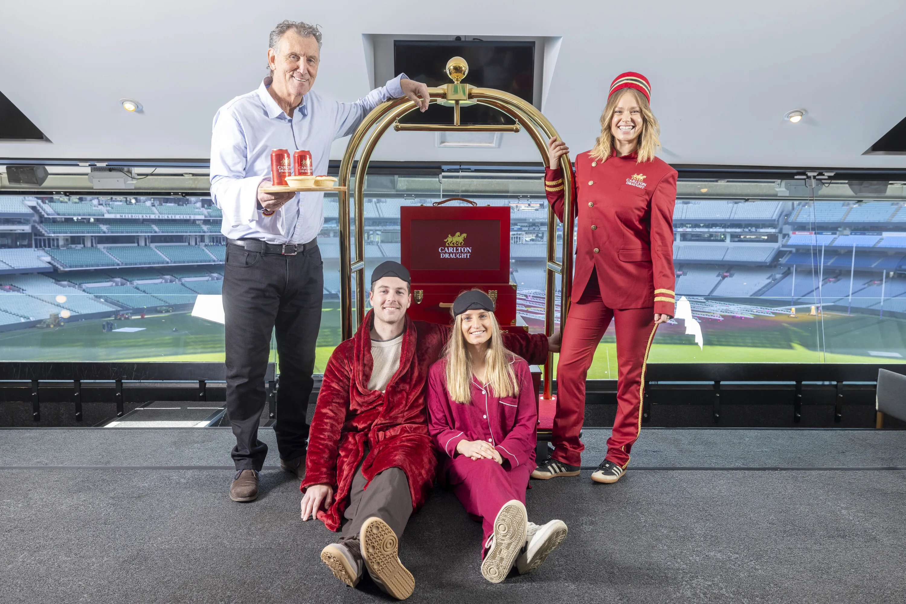 Four people pose in a suite overlooking the MCG.