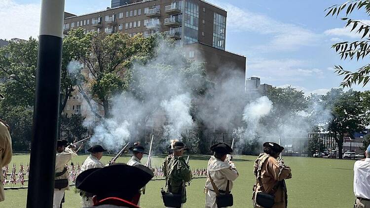 War re-enacters in costumes fire guns in an open park with lots of smoke following the shooting.