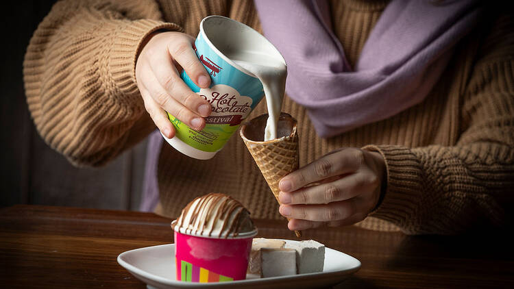A person pouring a hot chocolate into an ice cream cone.